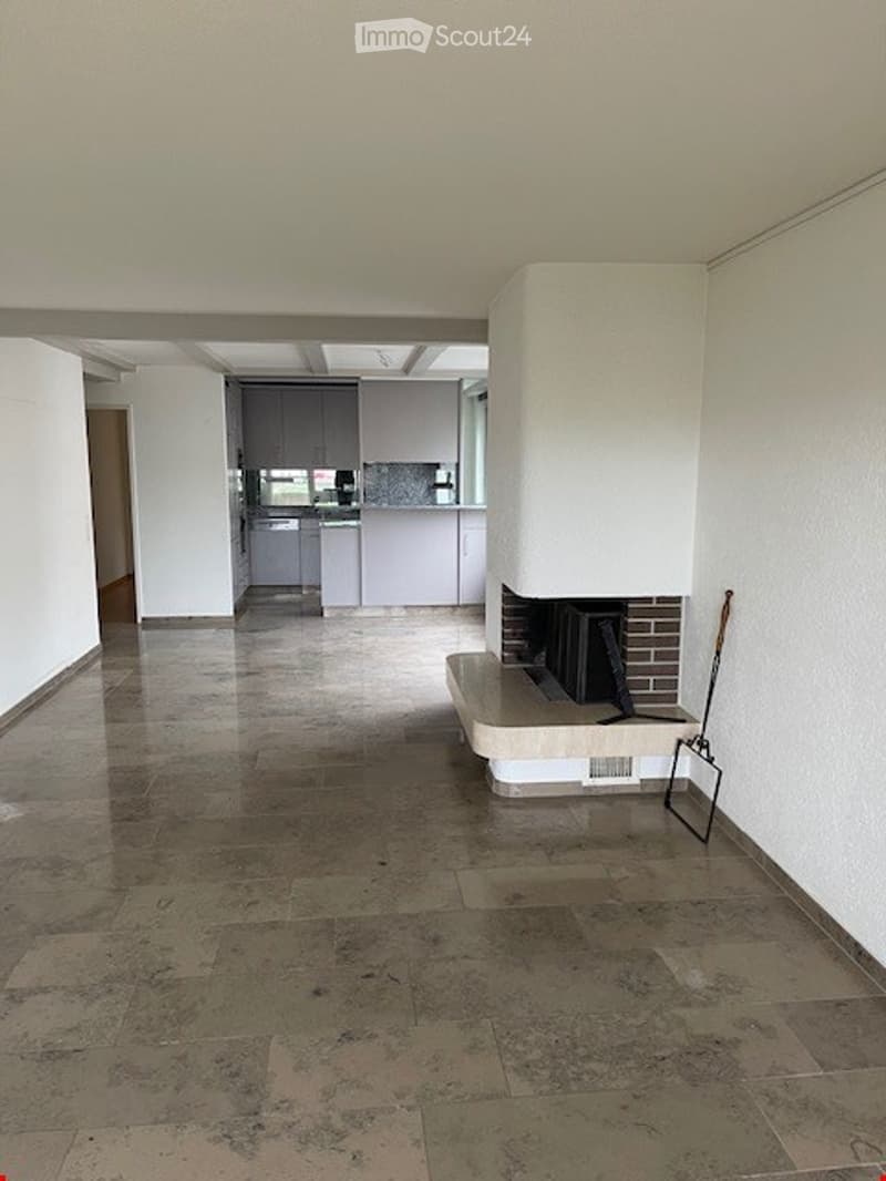 Empty living space with a fireplace, modern kitchen in the background, polished tile floor, and white walls.