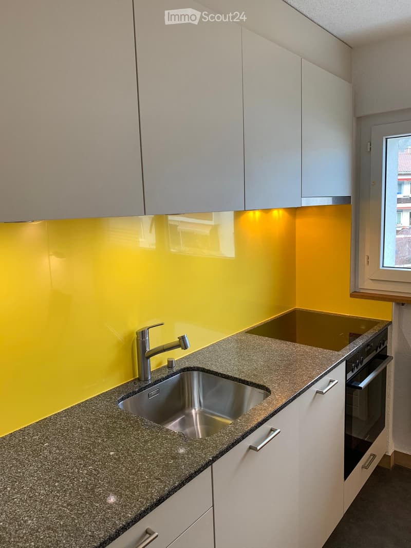 Modern kitchen with granite countertop, stainless steel sink, faucet, and built-in oven. Bright yellow backsplash and white cabinets.