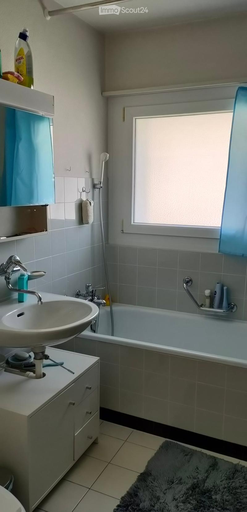 Modern bathroom with a white sink, bathtub, tiled walls, and a window. Includes a mirror, cabinet, and a towel on the wall.