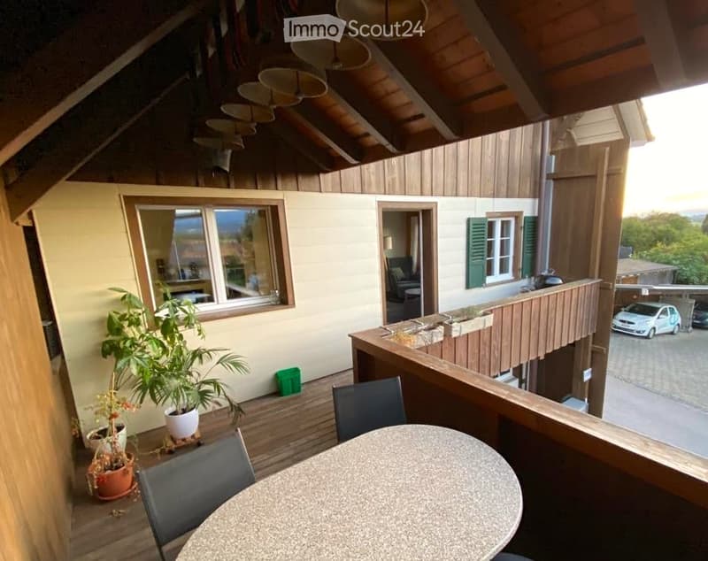 Balcony with wooden decking, round table, chairs, potted plants, and a view of the surrounding area.