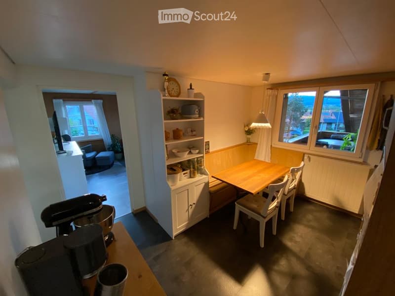 Cozy kitchen with a wooden dining table and chairs, white cabinets, a mixer, coffee maker, and decorative items on shelves.