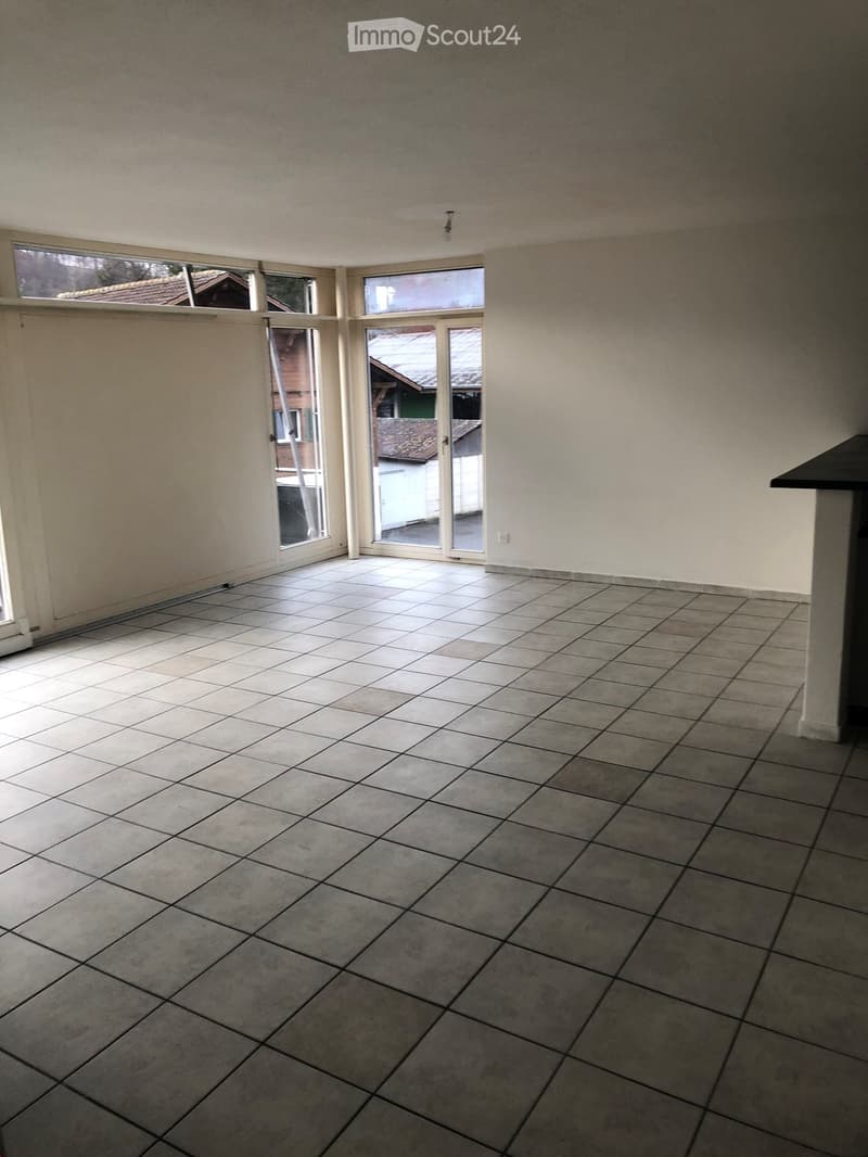 Empty room with tiled floor and large windows, featuring a sliding glass door leading outside.