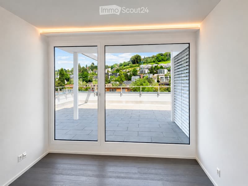 Empty room with white walls, wooden flooring, and large windows opening to a balcony with a scenic view.