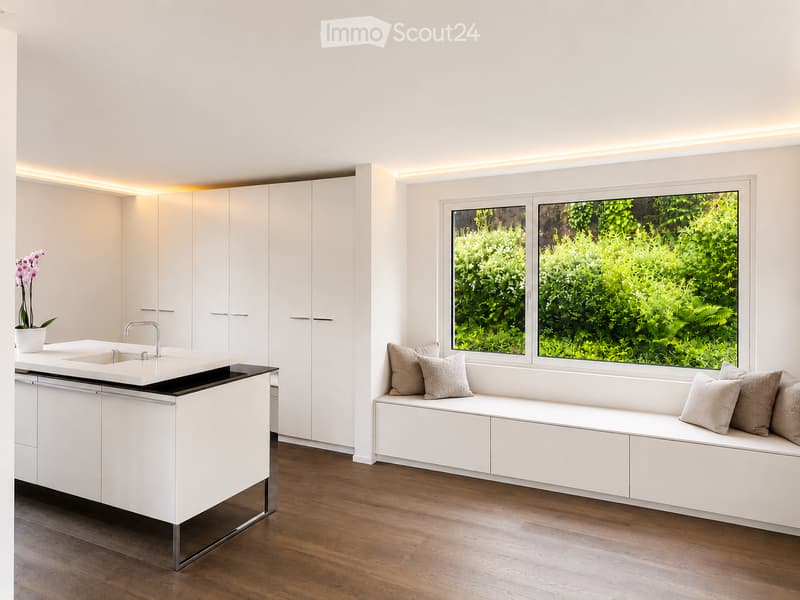 Modern kitchen with white cabinets, a built-in bench with pillows, a sink, and a vase with flowers on the counter.