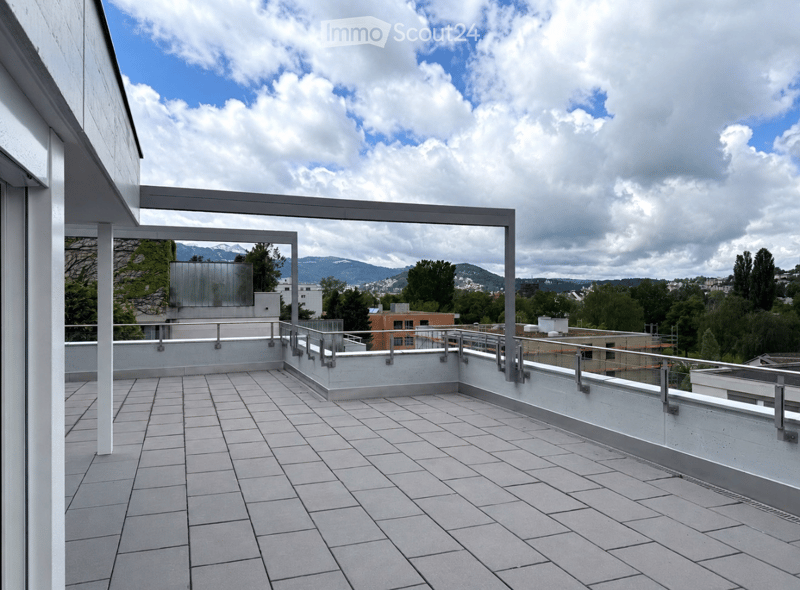 Modern rooftop terrace with tiled flooring, metal railings, and a scenic view of mountains and cityscape.