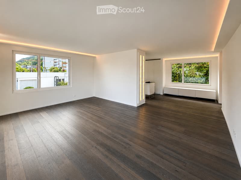 Empty room with dark wooden flooring, white walls, large windows with views, and built-in cabinetry.