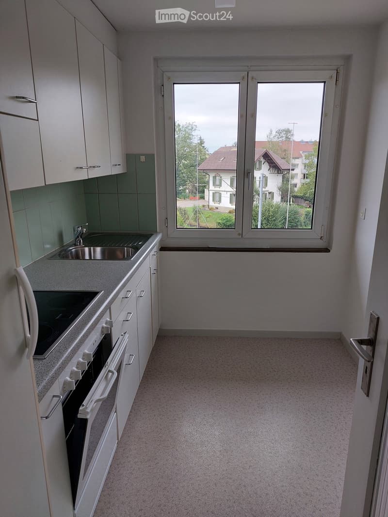 Modern kitchen with white cabinets, a sink, an oven, and a large window overlooking a residential area.