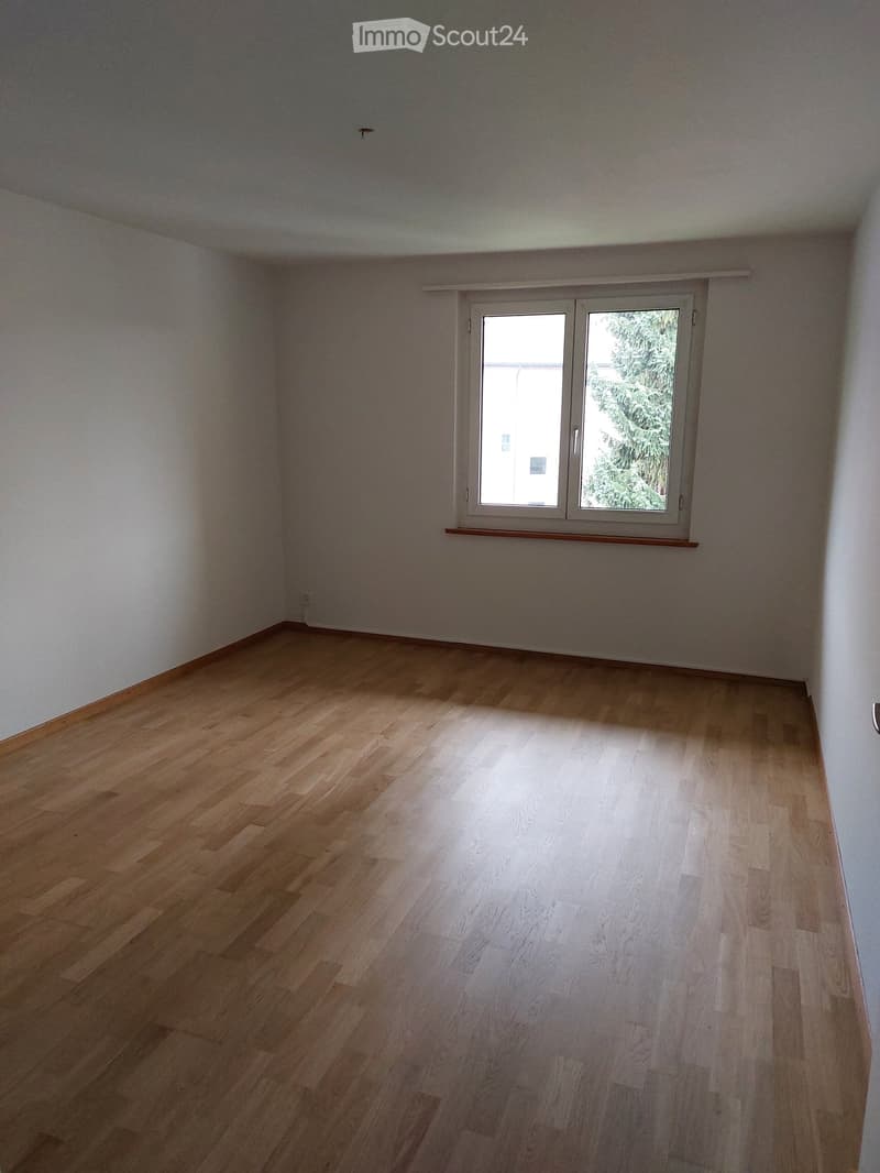 Empty room with light wooden flooring and white walls, featuring a single window with white frame and blinds.