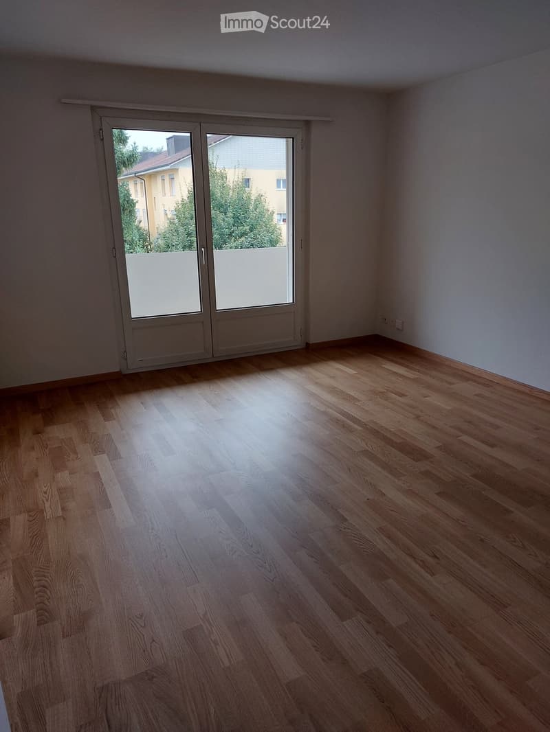 Empty room with wooden flooring and large sliding glass doors leading to a balcony or outdoor area.