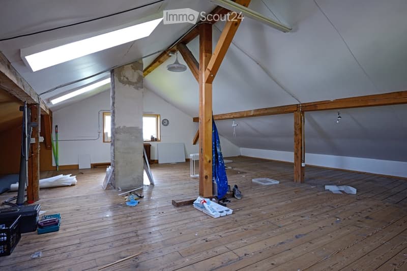 Empty attic space with wooden floors, exposed wooden beams, skylights, and minimal furnishings. Includes a small table, a radiator, and scattered construction materials.