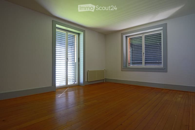 Empty room with wooden flooring, white walls, and two windows with shutters. A radiator is visible on one wall.