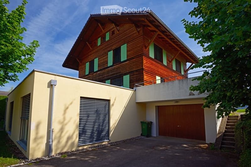 Two-story house with a raised ground floor, wooden upper level, and a garage.