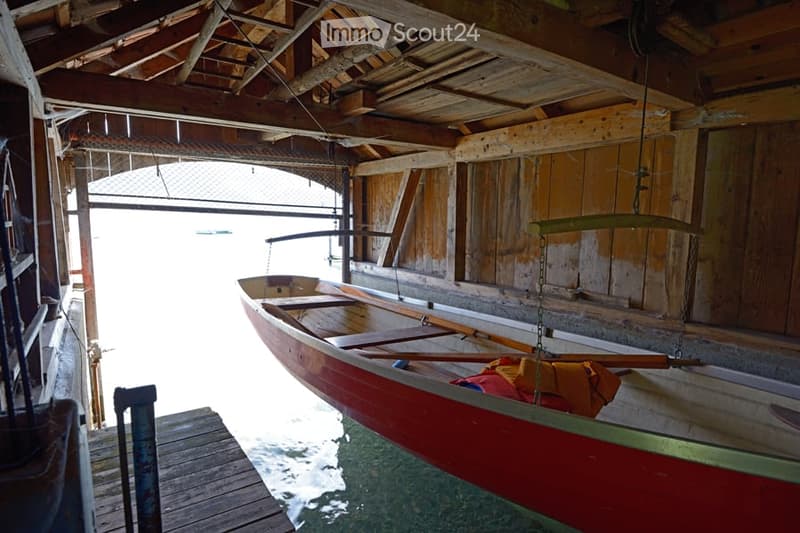 A wooden boathouse with a red canoe inside, wooden beams, and a view of water through the open doorway.