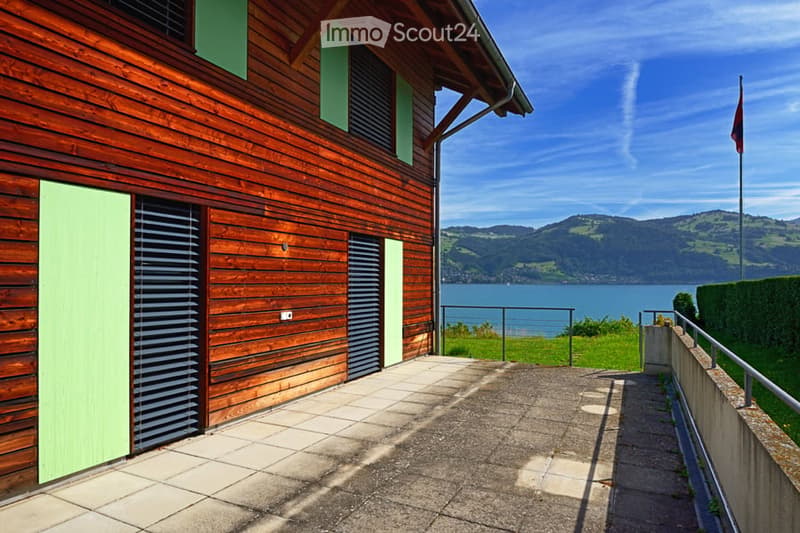 Wooden house exterior with green shutters, overlooking a lake and mountains.