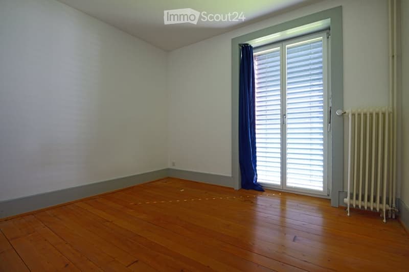Empty room with wooden flooring, white walls, a window with blinds, and a radiator.