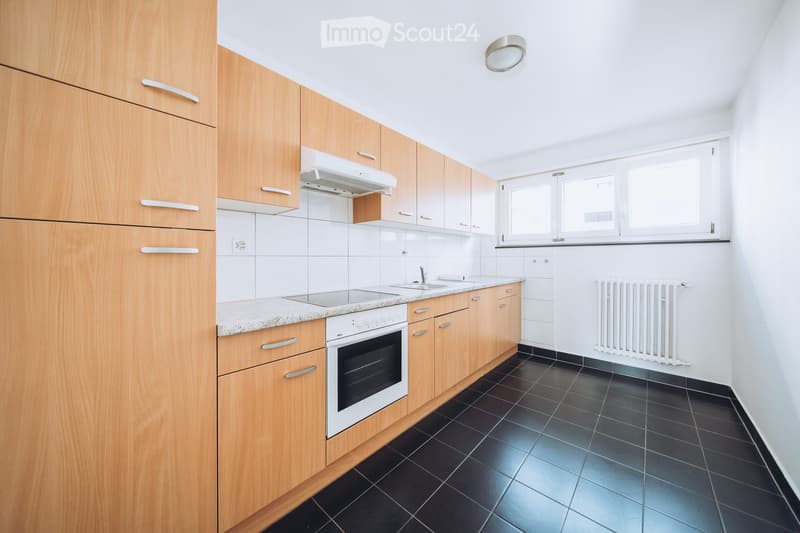 Modern kitchen with light wooden cabinets, granite countertop, black tiled floor, and built-in oven.