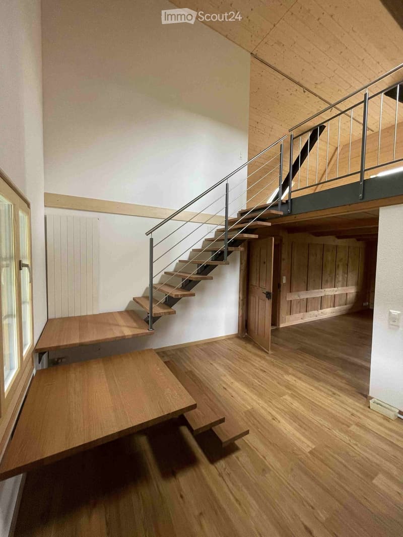 Corridor / Hallway. Modern hallway with wooden flooring, white walls, and a staircase with metal railing leading to an upper level. Features include a large window on the left and a door leading to another room on the right.