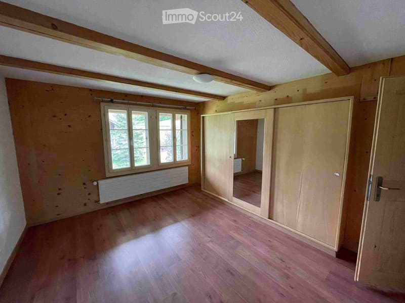 Unfurnished Room. Empty room with wooden flooring, exposed wooden beams on the ceiling, large windows, and a built-in closet with mirrored doors.