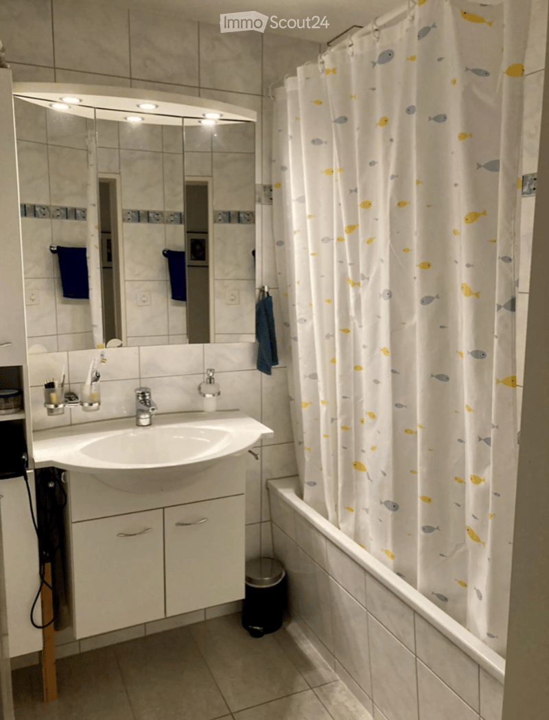 Modern bathroom with a white sink, large mirror, bathtub with a fish-patterned shower curtain, and neatly arranged towels.