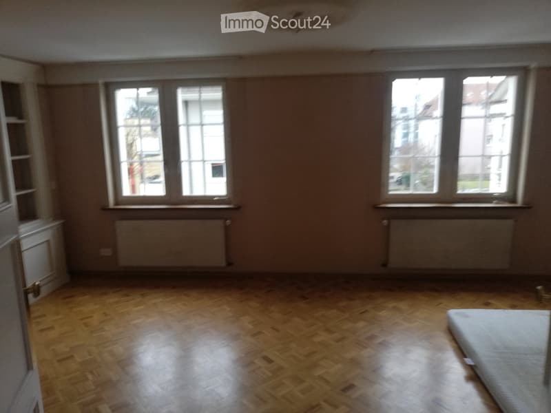 Empty room with wooden flooring, large windows, and radiators. No furniture or equipment present.