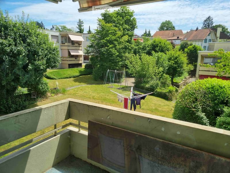 Balcony overlooking a well-maintained garden with a clothesline, swing set, and surrounding residential buildings.