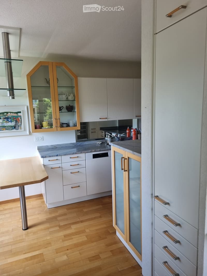 Modern kitchen with white cabinets, wooden accents, marble countertops, and a wooden table.