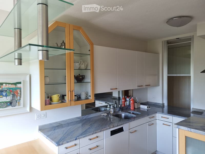 Modern kitchen with white cabinets, marble countertops, stainless steel sink, and glass display cabinet with teapots and cups.
