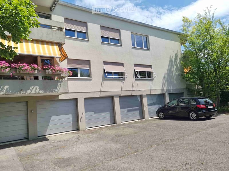Two-story house with multiple garage doors, large windows, and a balcony with flower boxes.