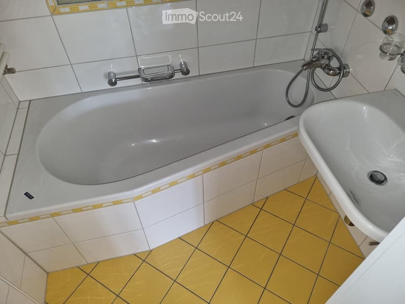 Bathroom with a large bathtub and a separate sink, featuring white tiles with yellow accents and a yellow tiled floor.