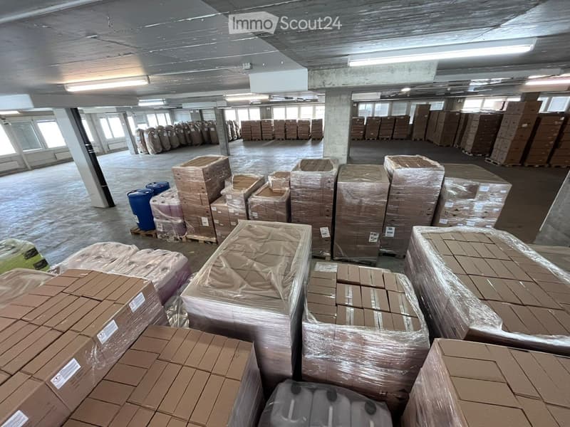 Storage space filled with numerous stacked boxes, wrapped in plastic. Barrels visible.