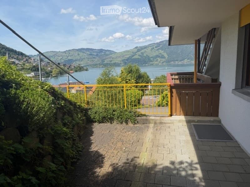 Balcony with brick tiles, yellow railing, overlooking a scenic lake and mountains.