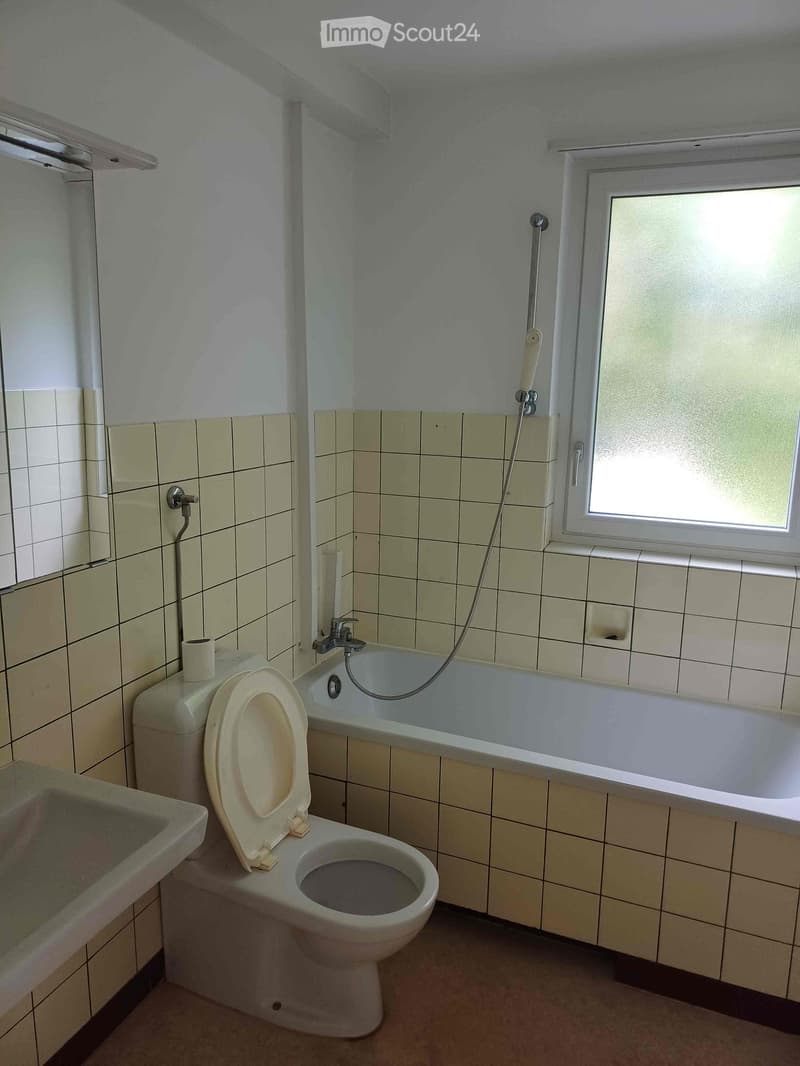 Bathroom with a toilet, bathtub, sink, and window. Light green tiles on walls and floor.