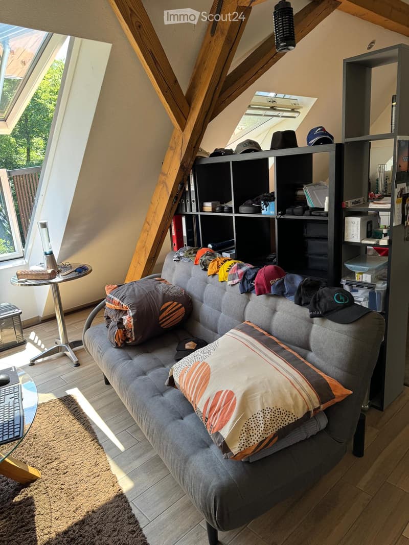 A cozy living room with a grey sofa, colorful pillows, a small round table, a keyboard on a glass surface, and a large bookshelf filled with various items.