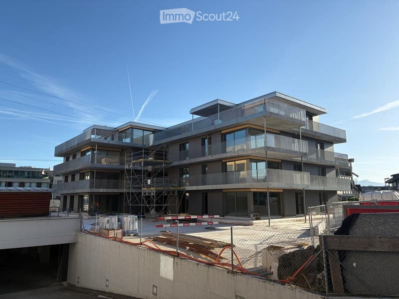 Modern multi-story residential building with balconies, large windows, and a contemporary design, partially under construction with scaffolding and fencing.