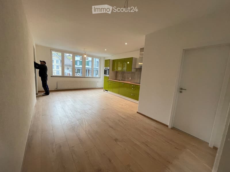 Empty kitchen with light wooden flooring, green cabinets, and a built-in oven. Large windows provide natural light.