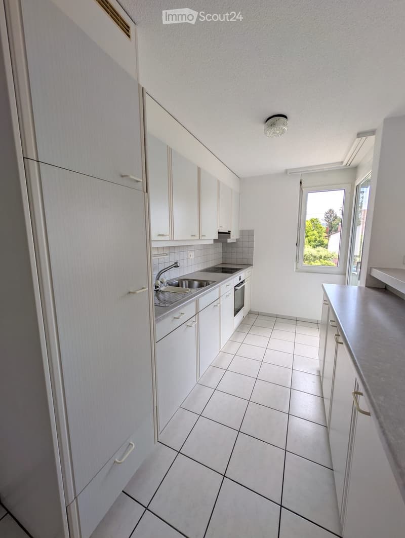 Modern kitchen with white cabinets, tiled floor, sink, faucet, and oven. Large window provides natural light.