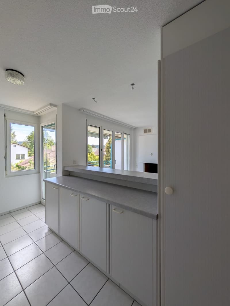 Modern kitchen with light grey cabinets, a countertop, and large windows offering a view of the outdoors.