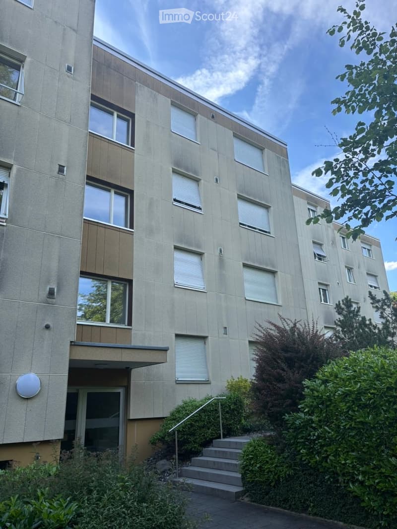 Modern multi-story apartment building with concrete facade, large windows, and raised entrance steps.