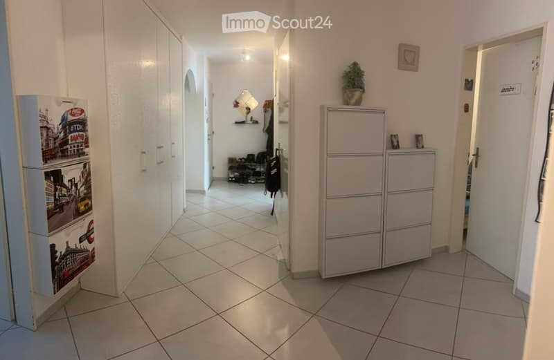 A clean, tiled hallway with white walls, a small plant on a cabinet, and a colorful refrigerator on the left side.