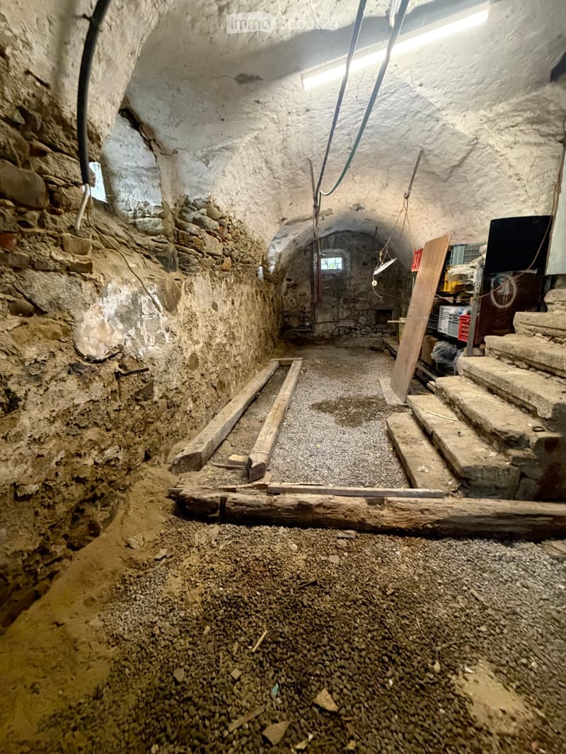 Underground corridor with stone walls, gravel floor, wooden planks, and a small staircase leading to another area.