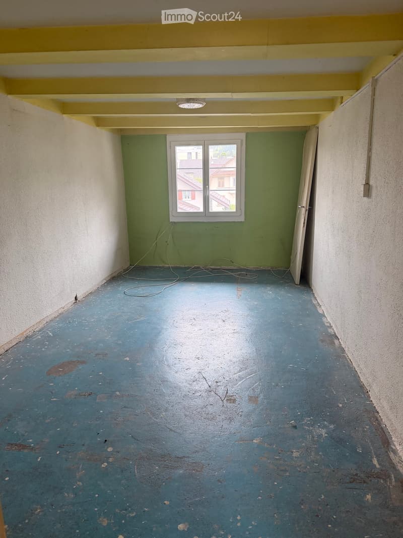 Empty room with blue concrete floor, green wall, white walls, window, and exposed electrical wires.