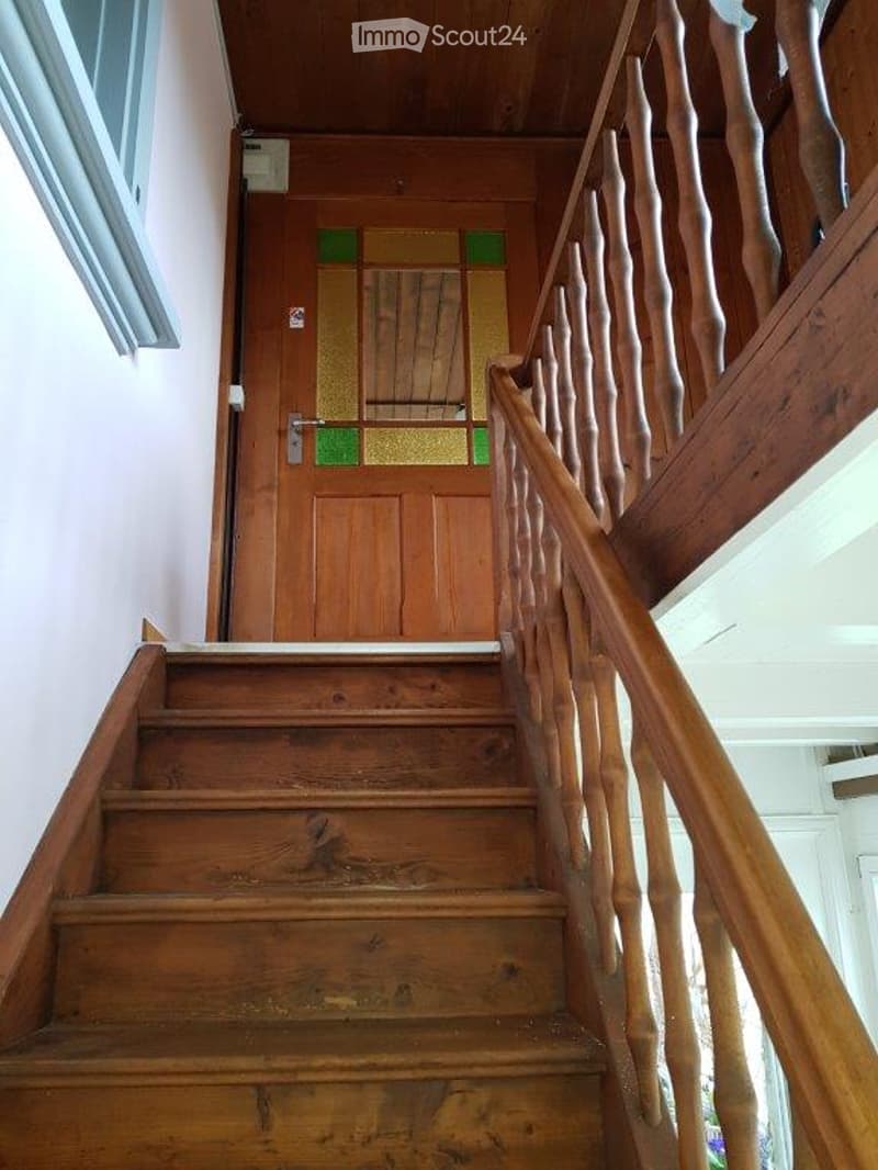 Wooden staircase with a handrail and a wooden door at the end, featuring a stained glass panel.