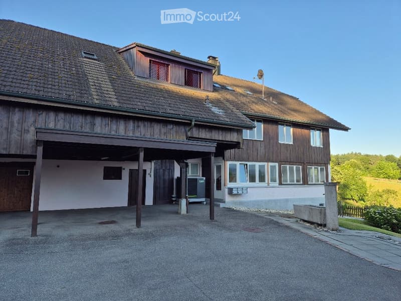 Two-story wooden house with a tiled roof, large garage, and multiple windows. The building features a mix of wood and plaster finishes.