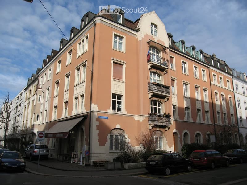 Multi-story residential building with peach-colored facade, white trim, multiple windows, and balconies. The building has a classic architectural style with ornate details and is situated on a street with parked cars and a sidewalk.
