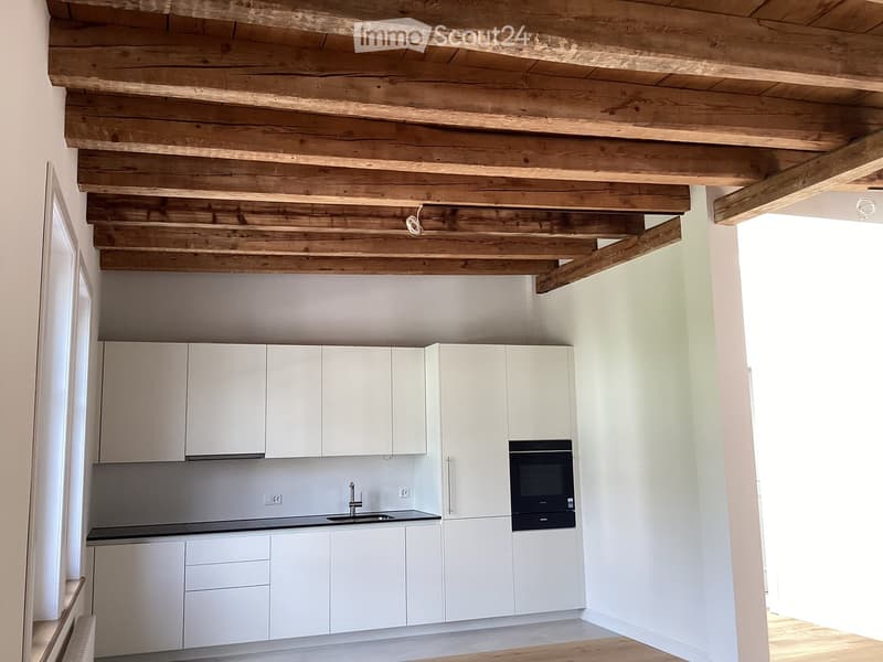 Modern kitchen with white cabinets, stainless steel sink, and built-in oven, featuring exposed wooden beams on the ceiling.