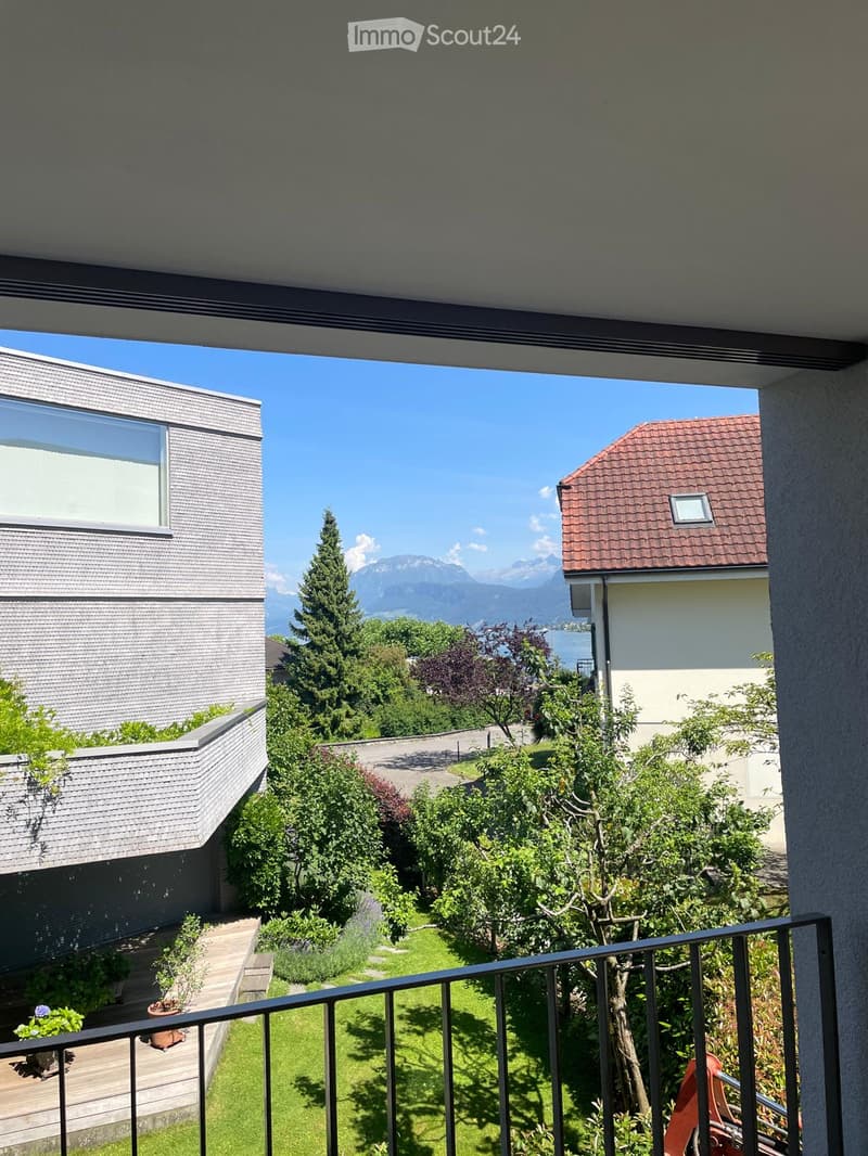 Balcony overlooking a well-maintained garden with various plants, trees, and a clear view of mountains in the background.