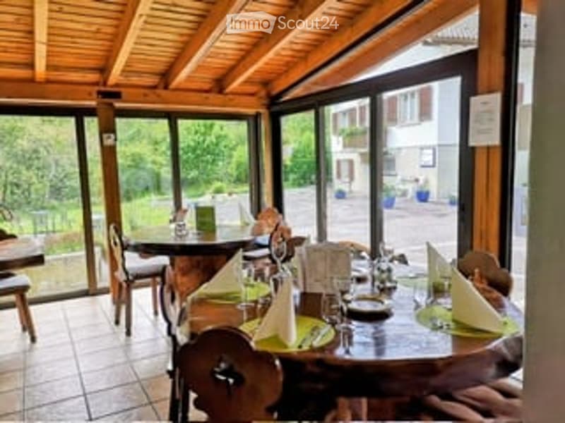 Brightly lit room with large windows, wooden tables and chairs, set with dishes and napkins, creating a cozy dining atmosphere.