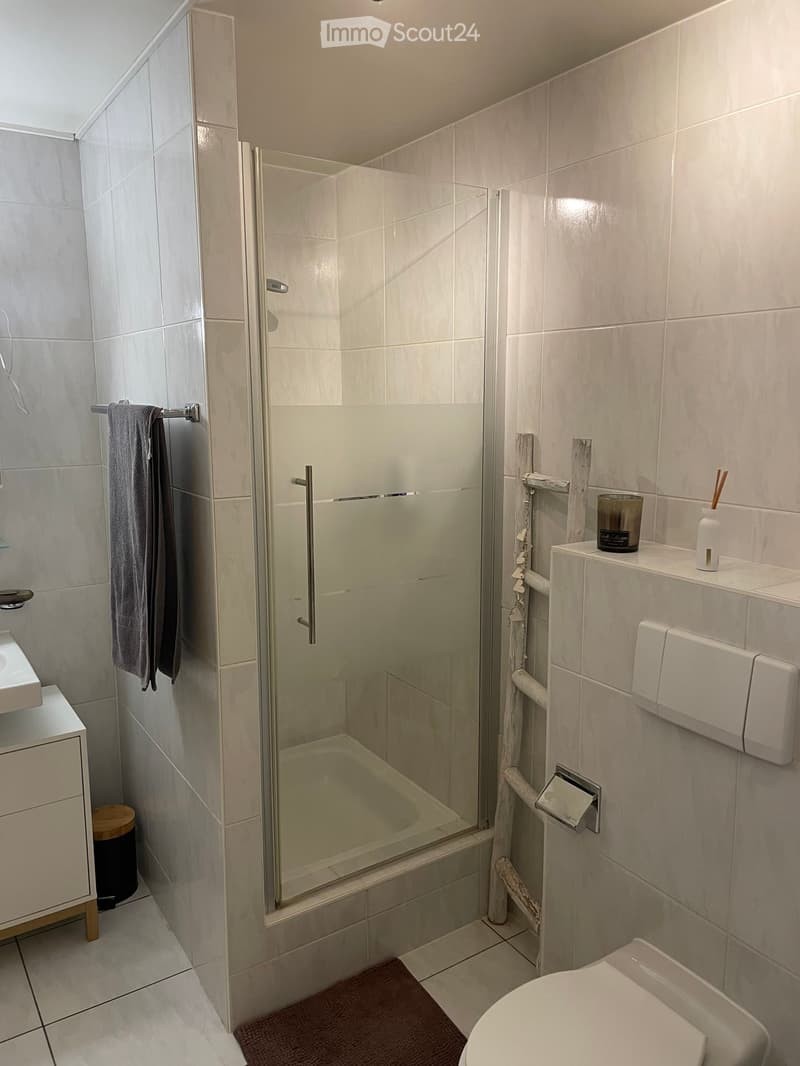 Modern bathroom with a glass-enclosed shower, white tiles, a sink, toilet, and a towel hanging on a rack.