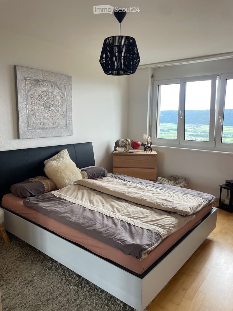 Modern bedroom with a large bed, nightstand, and a scenic view through large windows.