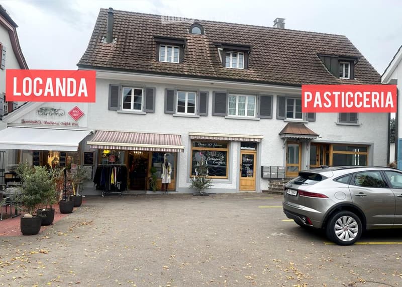 Two-story building with a tiled roof, multiple windows, and commercial storefronts including a café and a pastry shop.